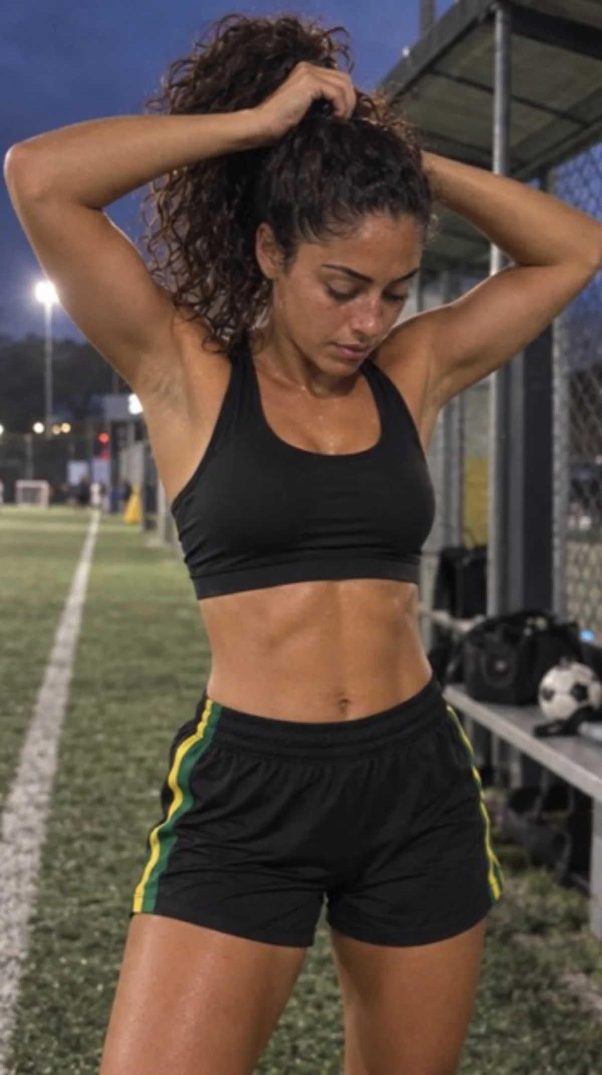 Camila Rios, a fictional virtual athlete, adjusting her hair beside a football field at night